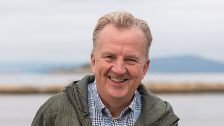 Mann som smiler med hav i bakgrunn. Foto