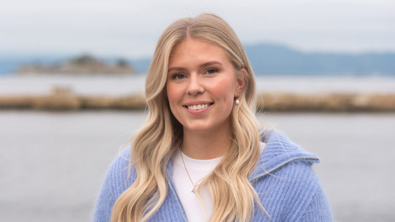 Dame som smiler med hav i bakgrunn. Foto