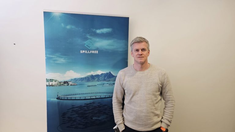 Mann som smiler foran reklameplakat. Foto