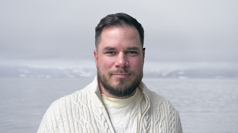 Mann som smiler med hav i bakgrunn. Foto