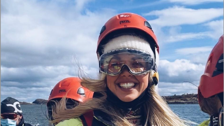 Dame som smiler med hav og himmel i bakgrunnen. Foto.