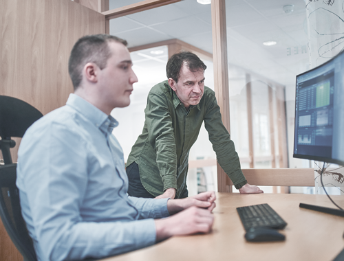 To menn lener seg over et skrivebord mot en pc